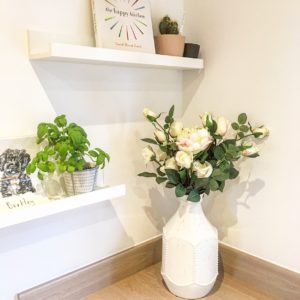 White vase of faux flowers against kitchen shelves 